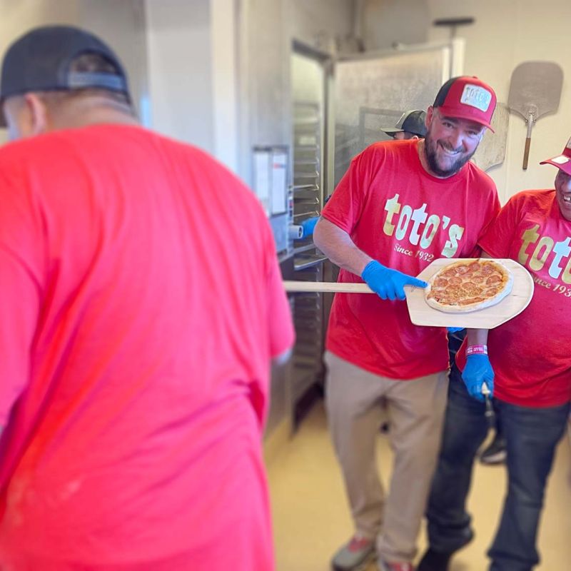 cook proudly shows handmade personal size pepperoni pizza on wood peel at Toto's Pizzeria concessions stand 315 at Levi's Stadium